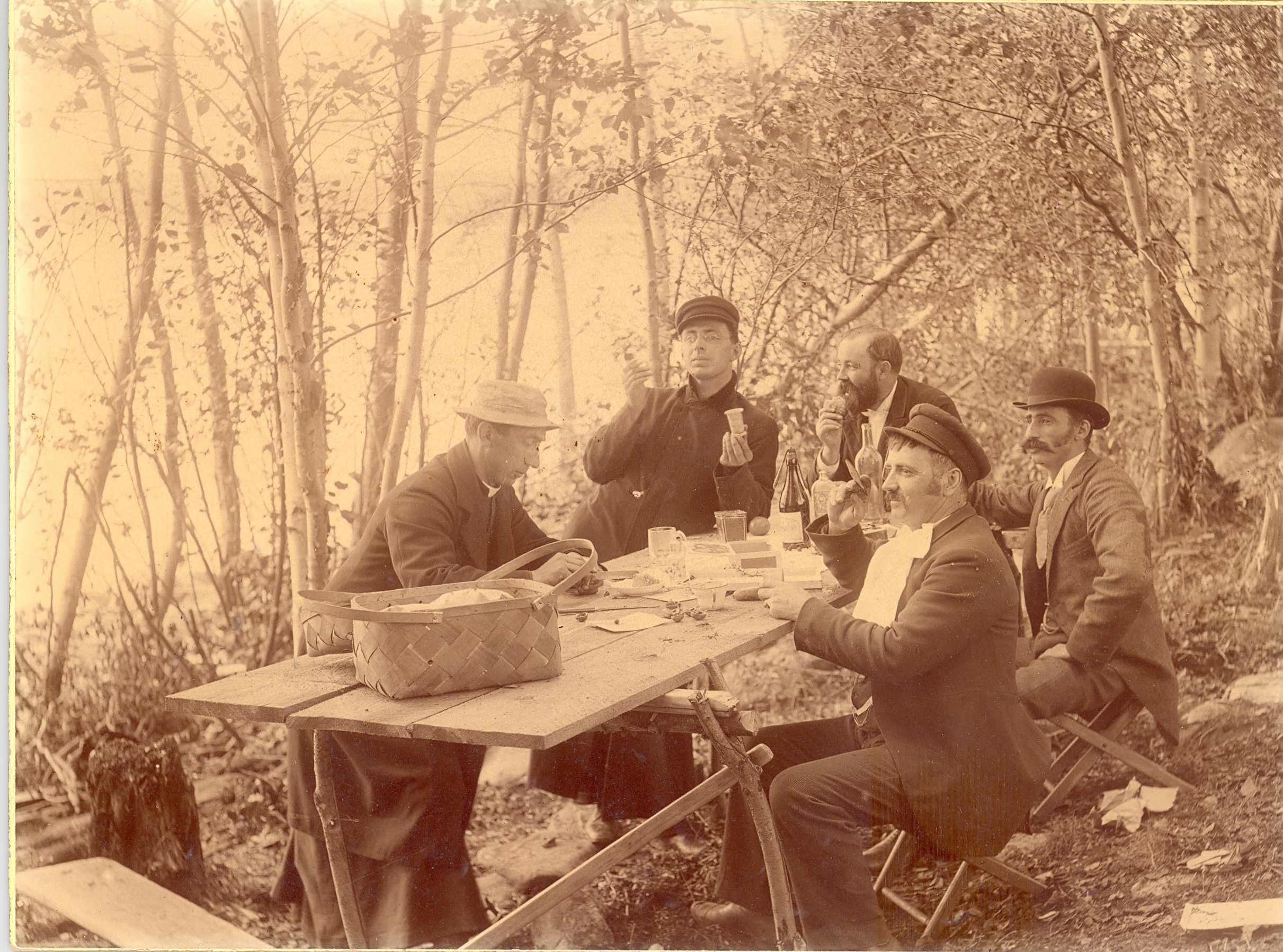 A group of men sitting around a table in the woodsDescription automatically generated with medium confidence